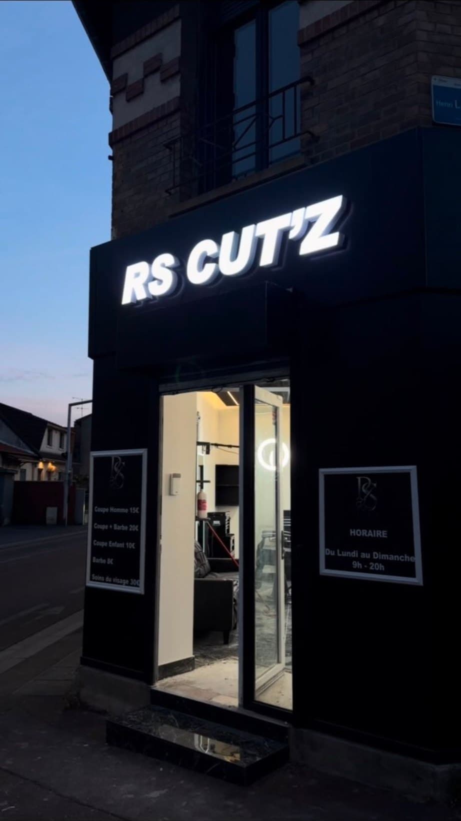 La devanture RS CUT'Z à la tombée de la nuit, enseigne lumineuse allumée